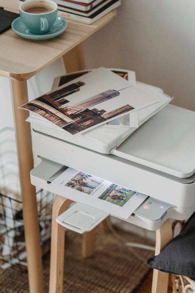 From above of images placed on printer on wooden table with cup of hot coffee at workplace