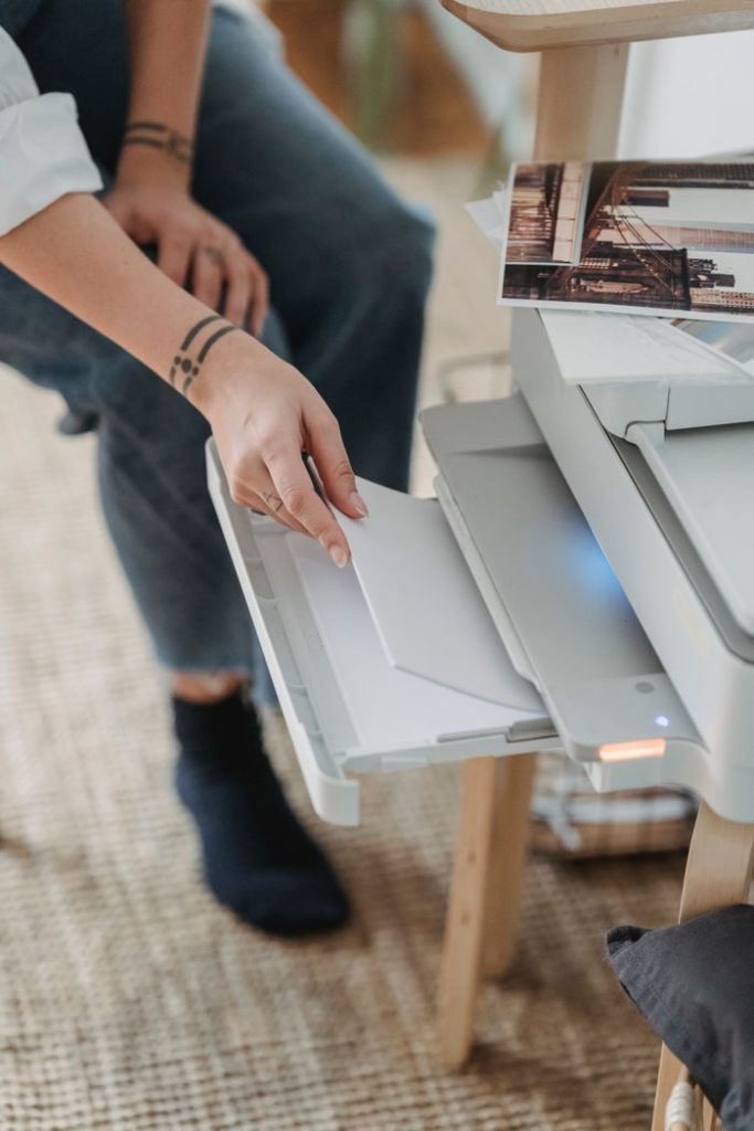 From above of crop unrecognizable female putting sheets of paper in printer for work